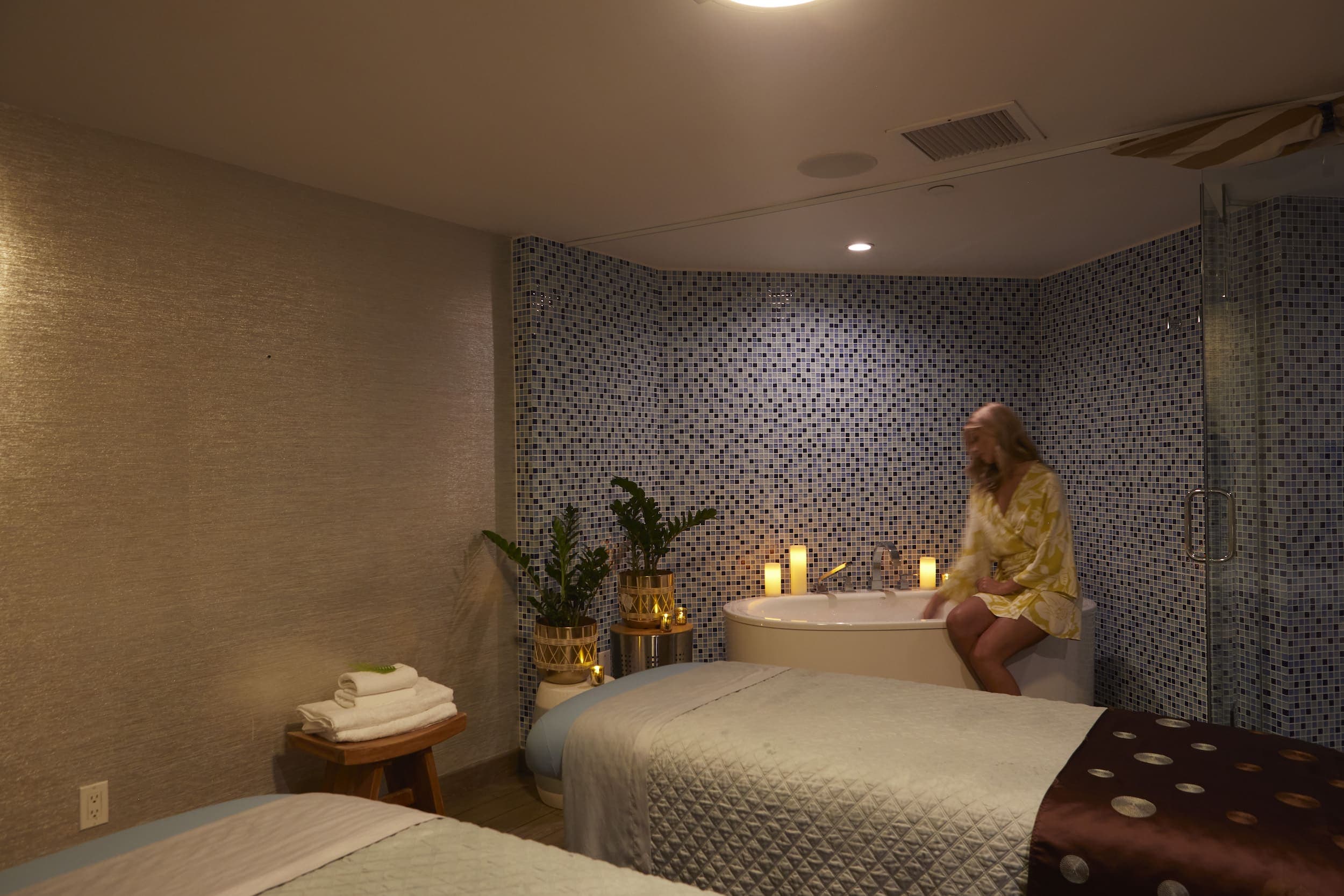 A woman sitting on the side of a soaker tub in a spa room at Kona Kai
