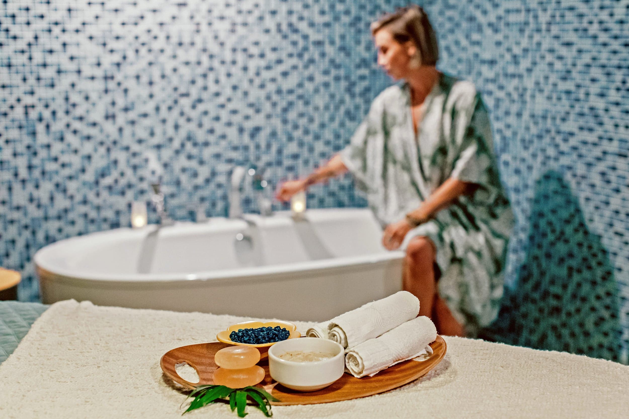 A woman at the spa sitting on the edge of the tub with a tray of blueberries, soap and towel