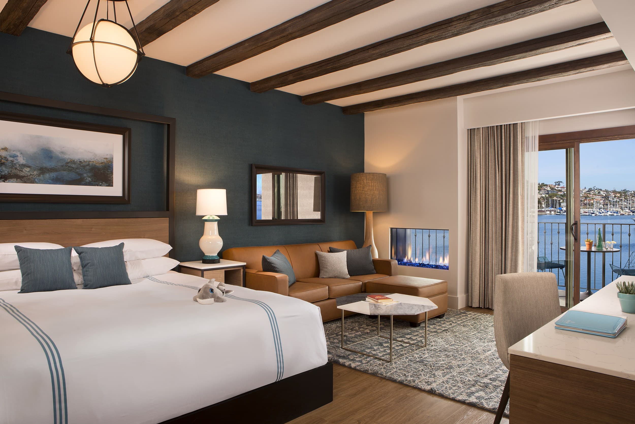 Kona Kai Resort & Spa fireplace junior suite in San Diego, featuring wood-beamed ceilings, a cozy seating area, and San Diego Bay views