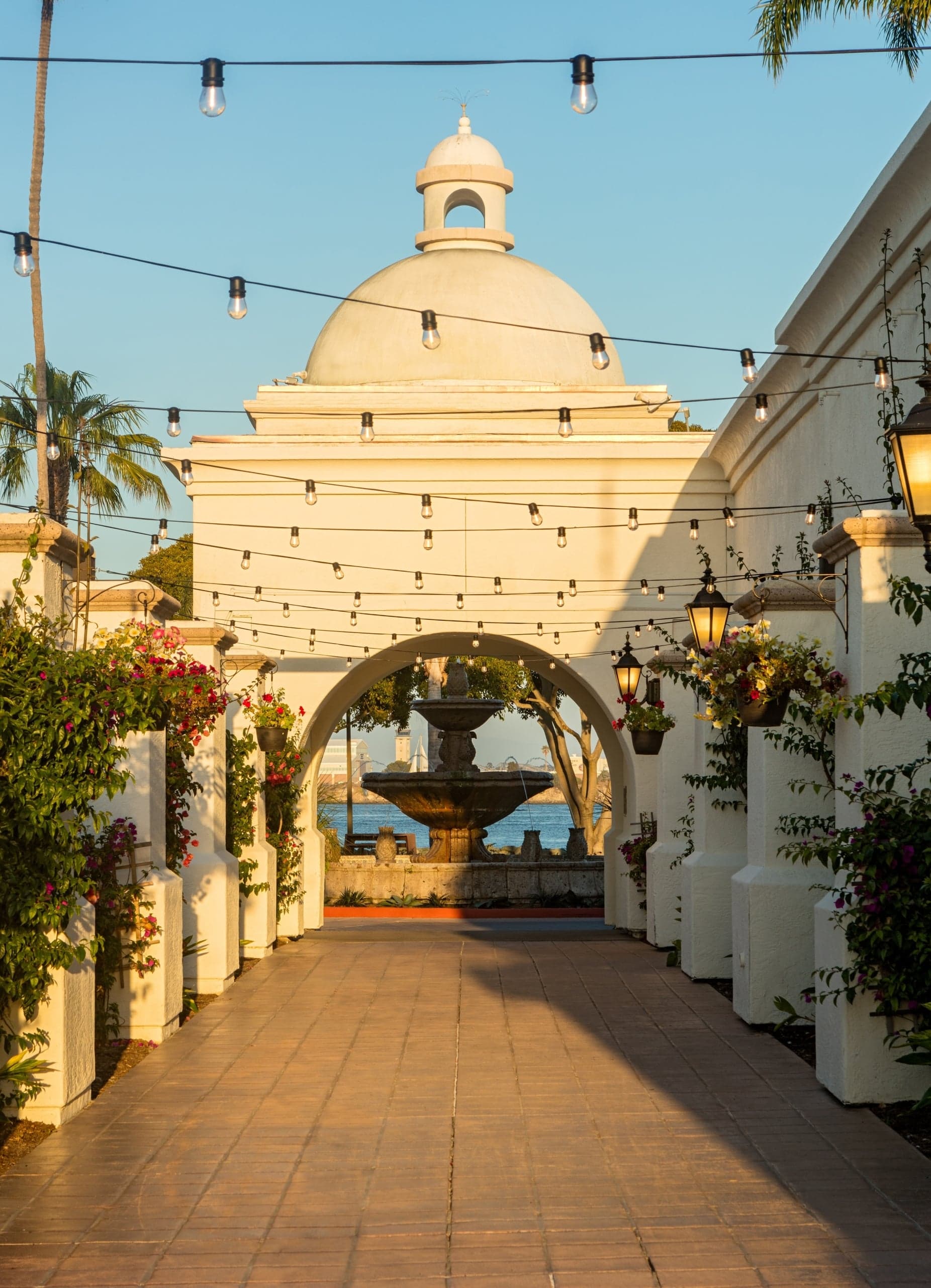 The Circle Patio at Kona Kai Resort, with a long walkway under a cupola that leads to a fountain, illuminated by string lights overhead