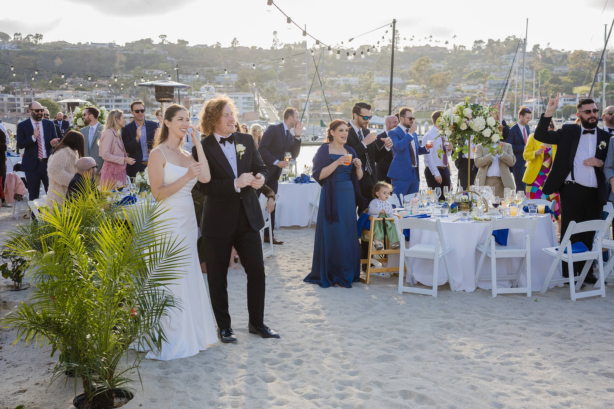 Bride and groom entering their waterfront beach wedding reception with guests and bay views at Kona Kai Resort & Spa on Shelter Island, San Diego