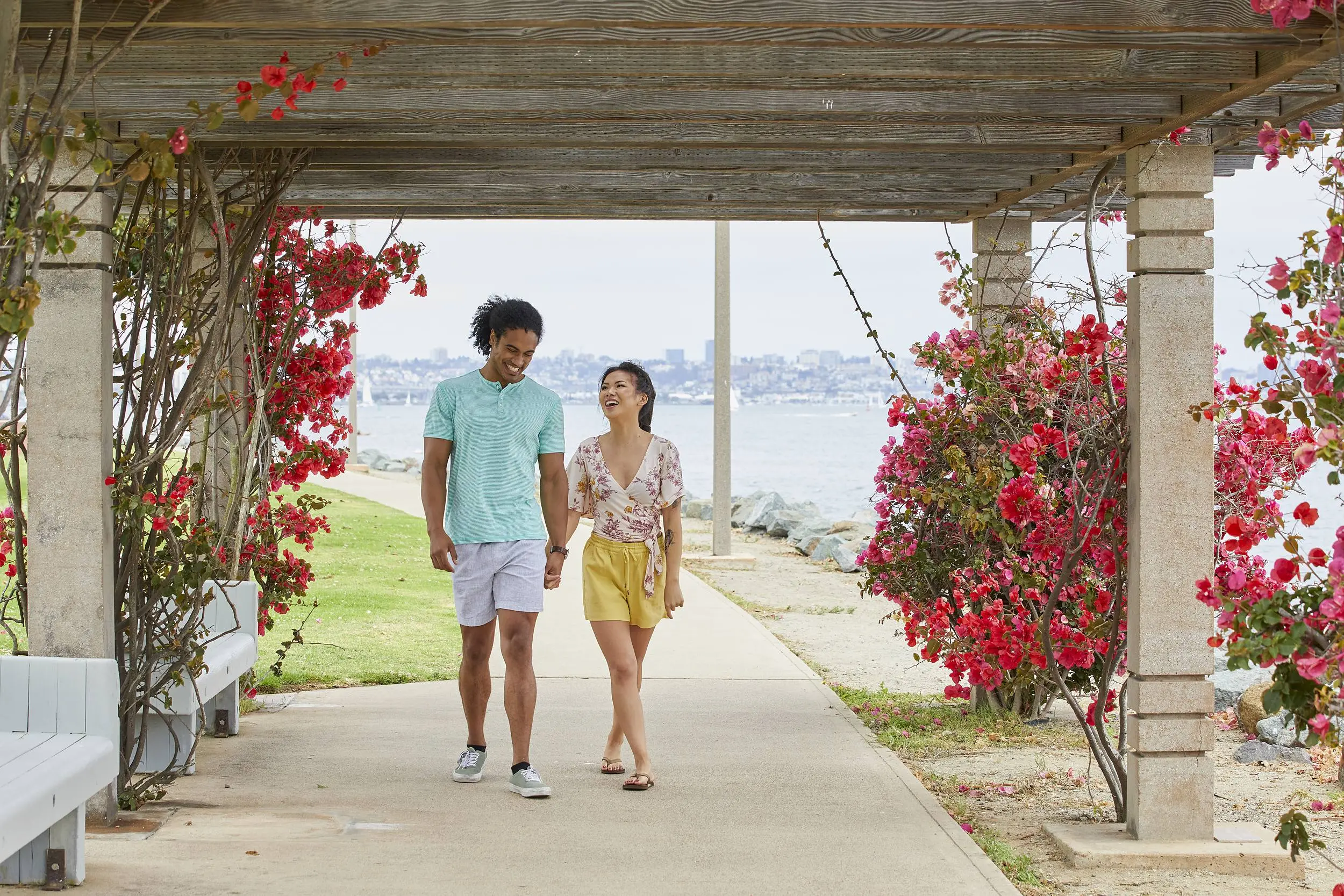 Couple strolling hand in hand along the bayfront pergola with bougainvillea at Kona Kai Resort & Spa on Shelter Island, San Diego