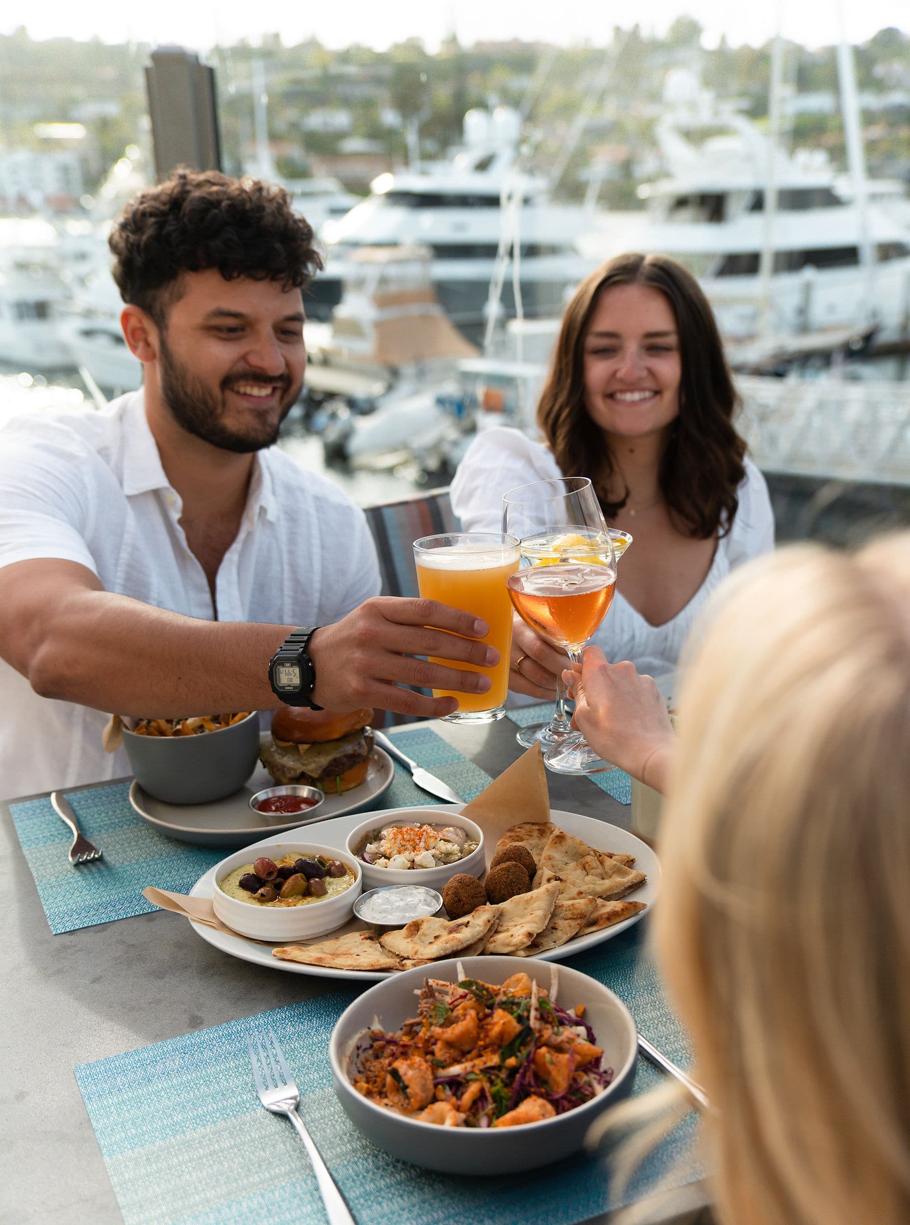 Friends toasting drinks over a mezze platter and marina views at Kona Kai Resort & Spa on Shelter Island in San Diego