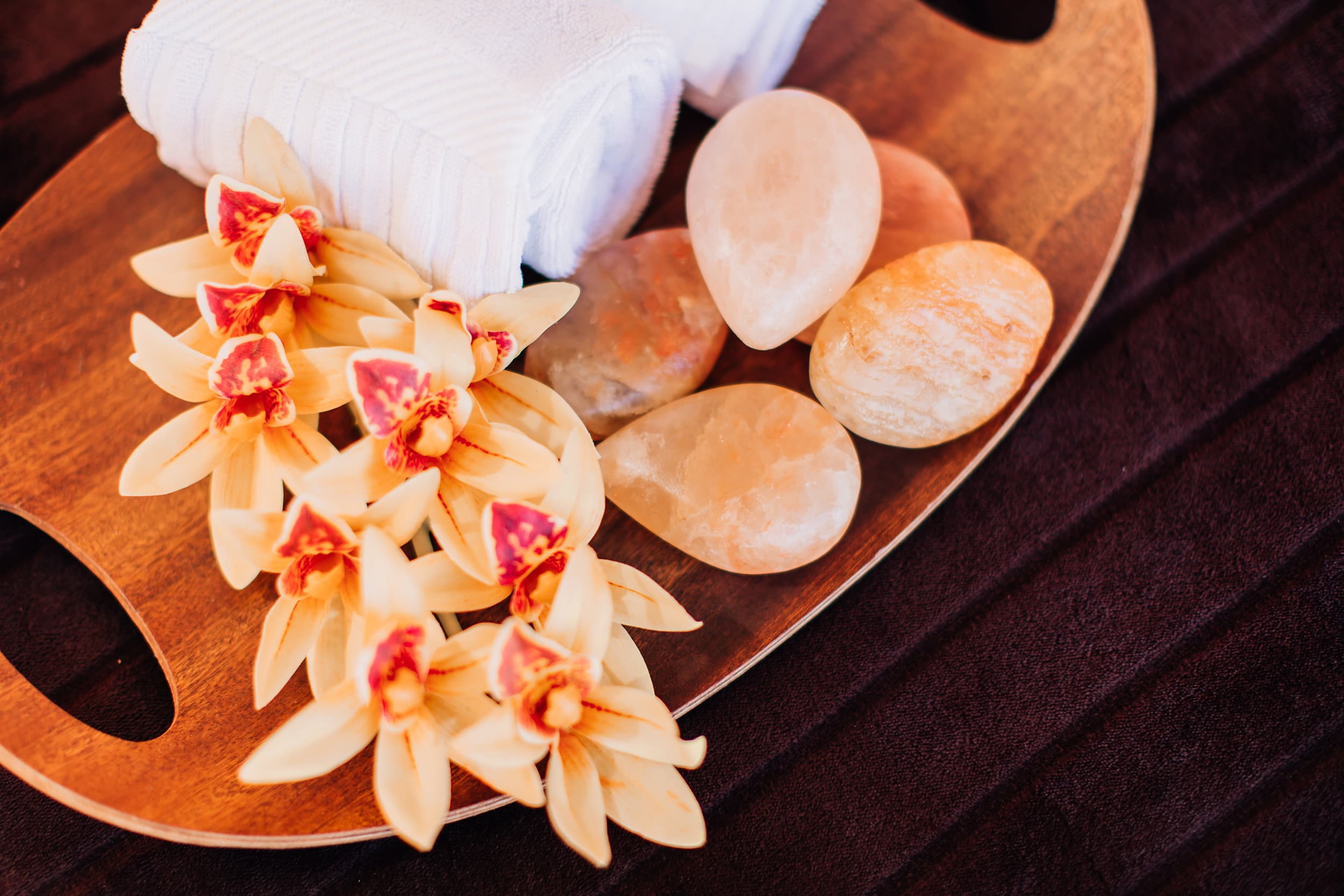 Cymbidium orchids, warm salt massage stones and a rolled white towel on a wood tray at the spa at Kona Kai Resort & Spa on Shelter Island, San Diego