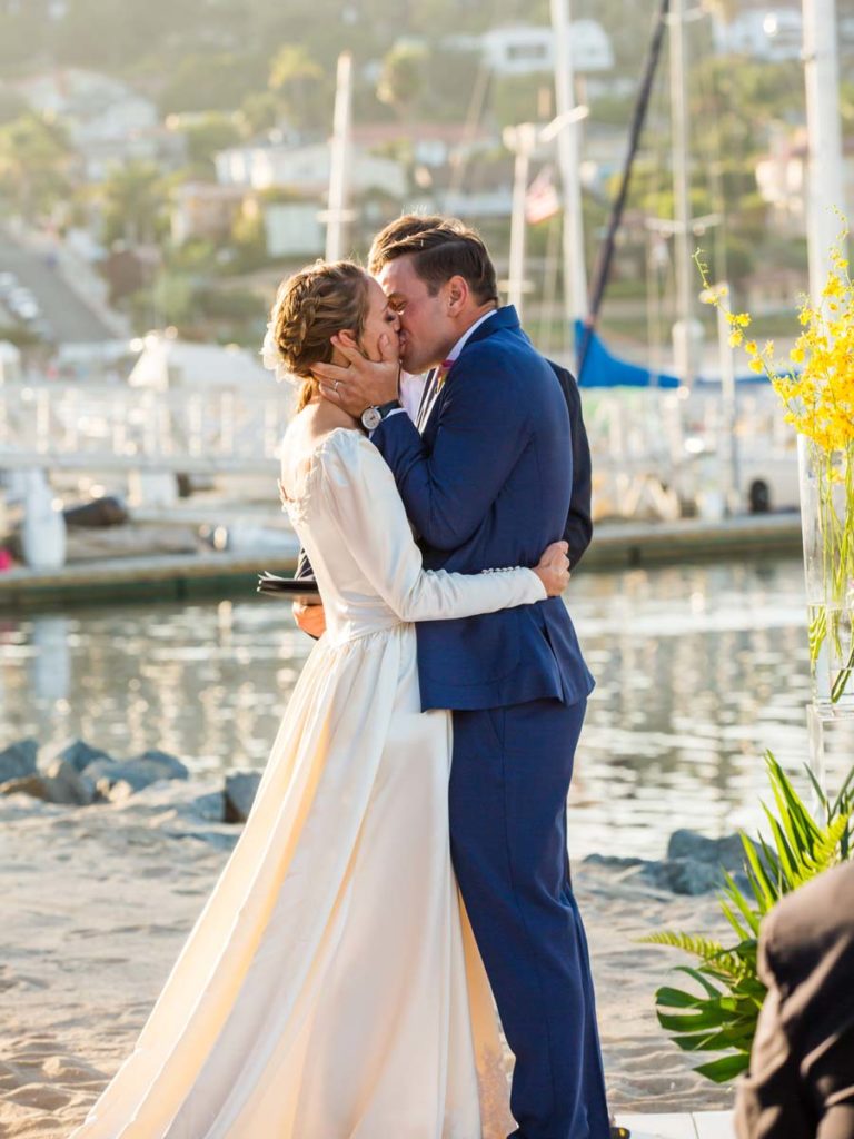 Bride and groom kiss by the marina.